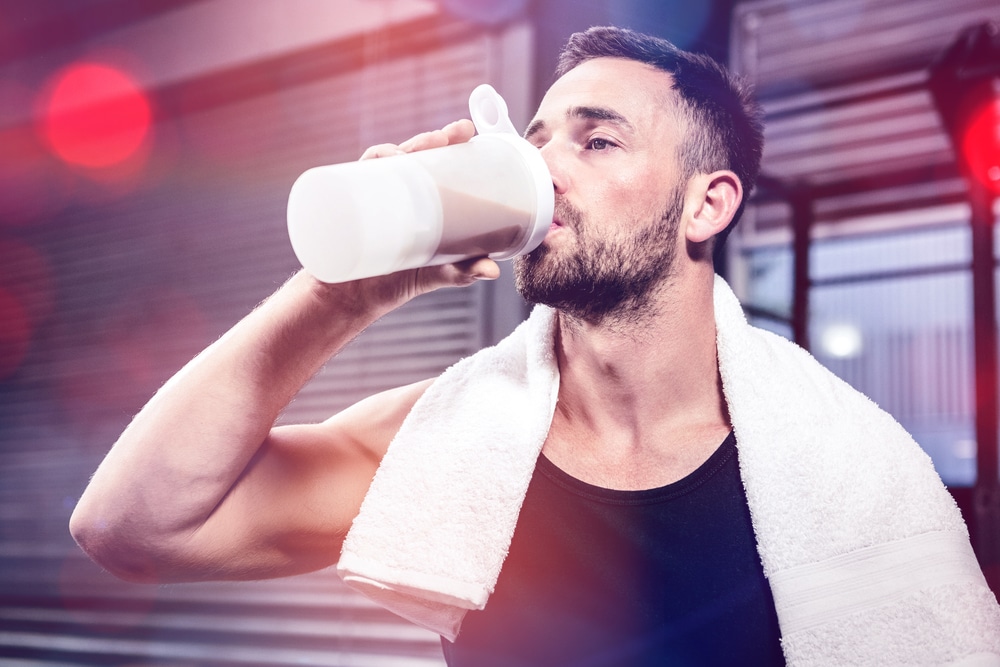 homme dans une salle de sport qui bois un shaker de protéine