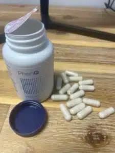 Flacon PhenQ ouvert et gélules sur table.